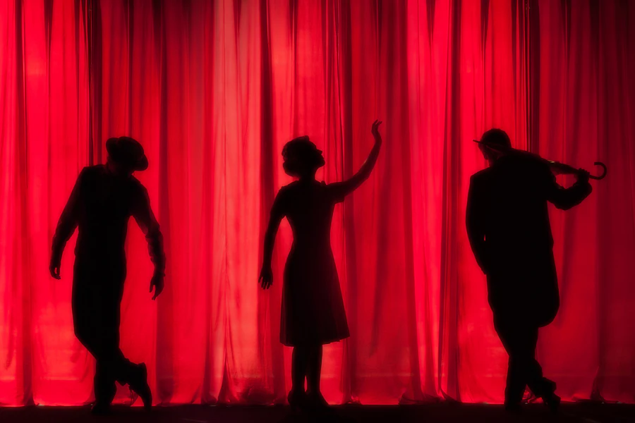 Silhouettes of three performers against a red curtain